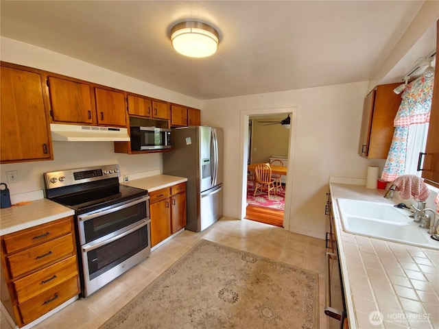 456 Upper Grand Ave, Hoquiam, WA 98550 - kitchen with stainless steel appliances, tile countertops, under cabinet range hood, brown cabinetry, and light tile patterned floors