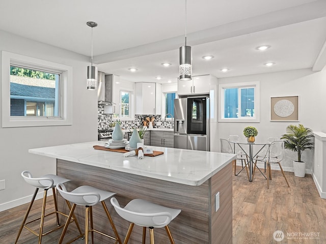 4853 42nd Ave SW, Seattle, WA 98116 - kitchen with stainless steel fridge, modern cabinets, wall chimney range hood, white cabinetry, and a kitchen bar