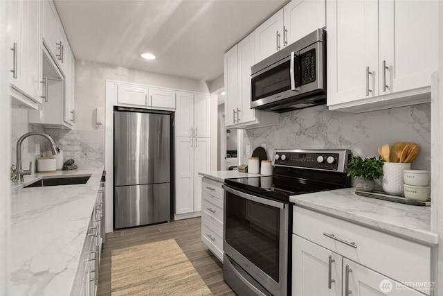 2219 Eastlake Ave E Unit 101, Seattle, WA 98102 - kitchen featuring appliances with stainless steel finishes, backsplash, white cabinets, light stone counters, and recessed lighting