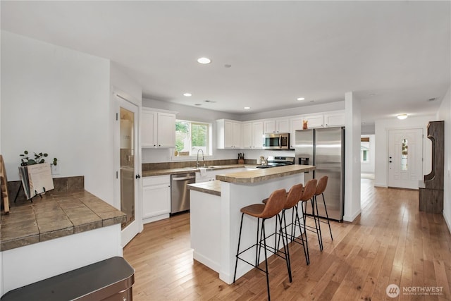1344 Foreman Rd, Dupont, WA 98327 - kitchen featuring appliances with stainless steel finishes, a kitchen bar, white cabinetry, light wood finished floors, and a kitchen island