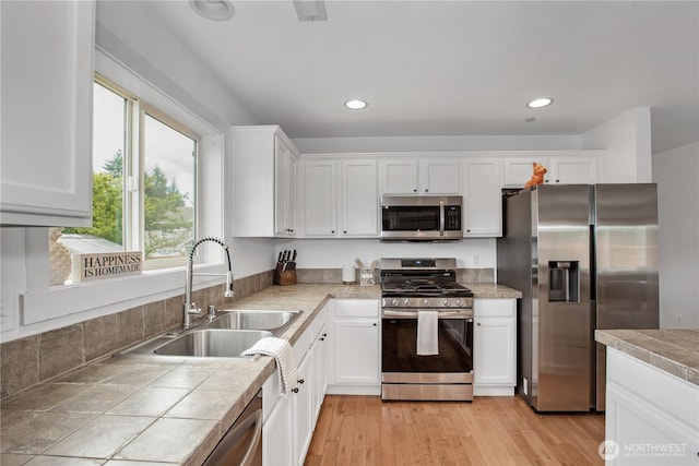 1344 Foreman Rd, Dupont, WA 98327 - kitchen with appliances with stainless steel finishes, white cabinets, tile countertops, recessed lighting, and light wood-style flooring