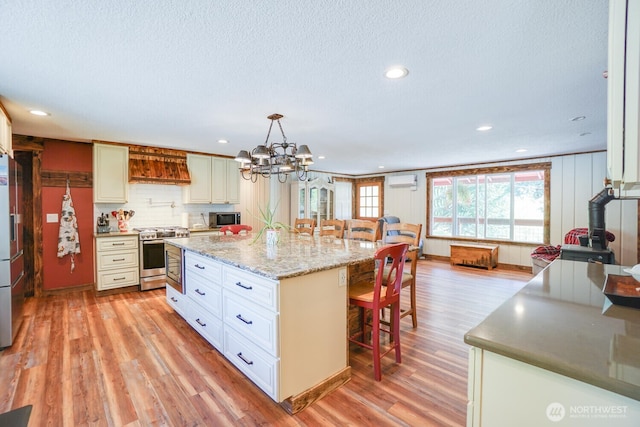19910 NE 356th St, Yacolt, WA 98675 - kitchen with stainless steel appliances, custom range hood, a kitchen breakfast bar, light wood finished floors, and a chandelier