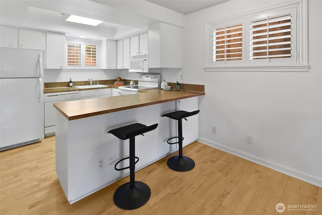 4444 44th Ave SW Unit 101, Seattle, WA 98116 - kitchen featuring white appliances, a peninsula, light wood finished floors, white cabinetry, and a breakfast bar area