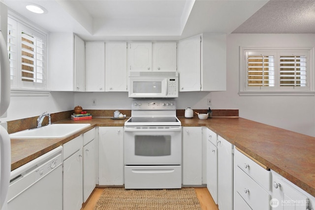 4444 44th Ave SW Unit 101, Seattle, WA 98116 - kitchen featuring white appliances, white cabinets, light wood-type flooring, and a tray ceiling