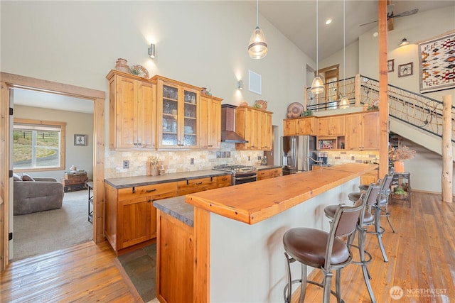 95 Horizon Ln, Chelan, WA 98816 - kitchen featuring high vaulted ceiling, appliances with stainless steel finishes, butcher block counters, wall chimney range hood, and a breakfast bar area