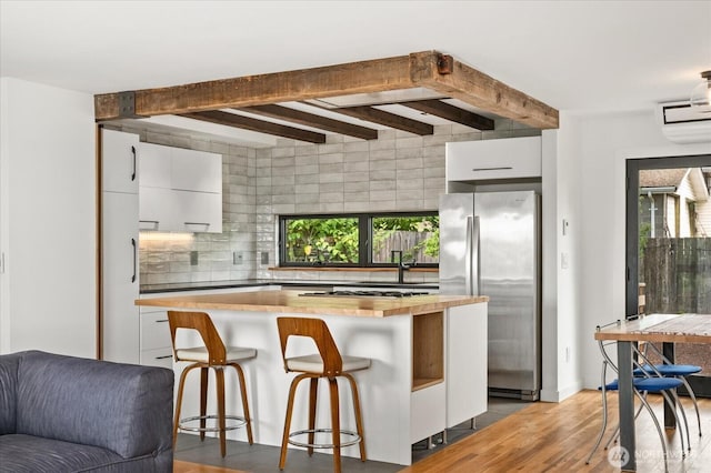 6024 Gould Ave S, Seattle, WA 98108 - kitchen with appliances with stainless steel finishes, white cabinets, beamed ceiling, tasteful backsplash, and light wood-style floors