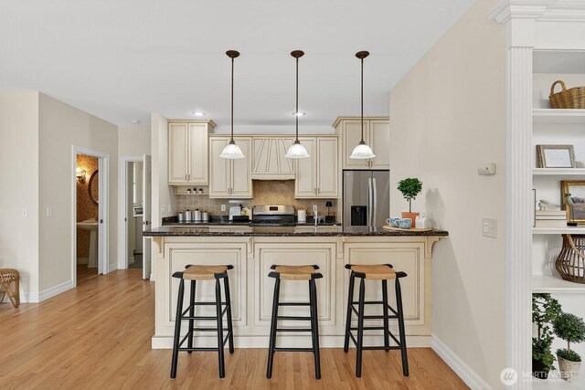 2414 42nd Pl, Anacortes, WA 98221 - kitchen with stainless steel appliances, cream cabinetry, a breakfast bar, decorative backsplash, and light wood-type flooring