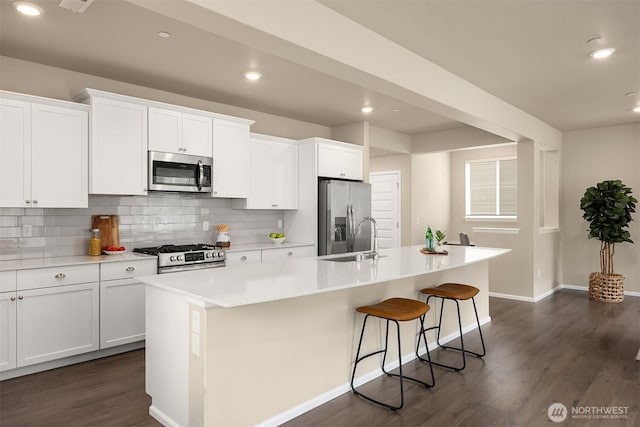 1312 Baker Heights Loop, Bremerton, WA 98312 - kitchen featuring appliances with stainless steel finishes, a kitchen island with sink, dark wood finished floors, decorative backsplash, and white cabinets