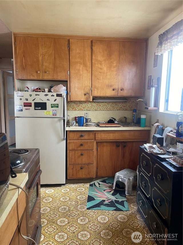 5006 N 28th, Tacoma, WA 98407 - kitchen with freestanding refrigerator, stainless steel electric stove, brown cabinetry, light countertops, and backsplash