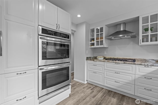 13002 145th St E, Puyallup, WA 98374 - kitchen with appliances with stainless steel finishes, wall chimney exhaust hood, light wood-style floors, glass insert cabinets, and recessed lighting