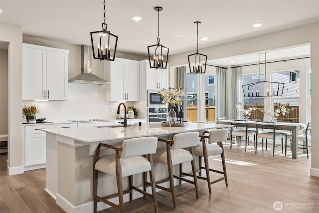 20259 145th St E Unit 856, Bonney Lake, WA 98391 - kitchen featuring wall chimney range hood, a chandelier, appliances with stainless steel finishes, a center island with sink, and light wood finished floors