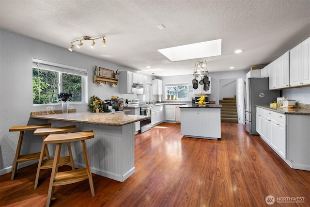 6621 125th Street Ct E, Puyallup, WA 98373 - kitchen with appliances with stainless steel finishes, a skylight, a peninsula, a textured ceiling, and white cabinets