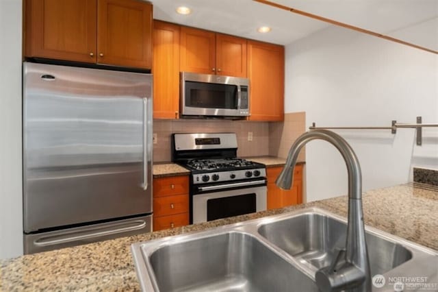 1420 Terry Ave Unit 907, Seattle, WA 98101 - kitchen with appliances with stainless steel finishes, brown cabinetry, decorative backsplash, recessed lighting, and light stone countertops