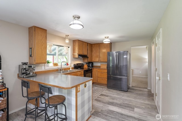 7649 Mcdougal Ave NE, Moses Lake, WA 98837 - kitchen featuring freestanding refrigerator, black electric range oven, a peninsula, brown cabinets, and light wood-style floors