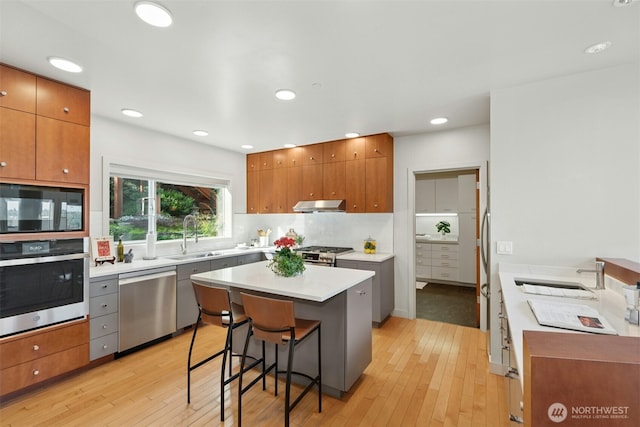 8812 NE 117th Pl, Kirkland, WA 98034 - kitchen with stainless steel appliances, light wood-type flooring, brown cabinets, a kitchen island, and a kitchen breakfast bar