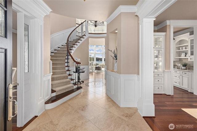 8071 W Mercer Way, Mercer Island, WA 98040 - tiled entryway with stairway, crown molding, a chandelier, a wainscoted wall, and decorative columns