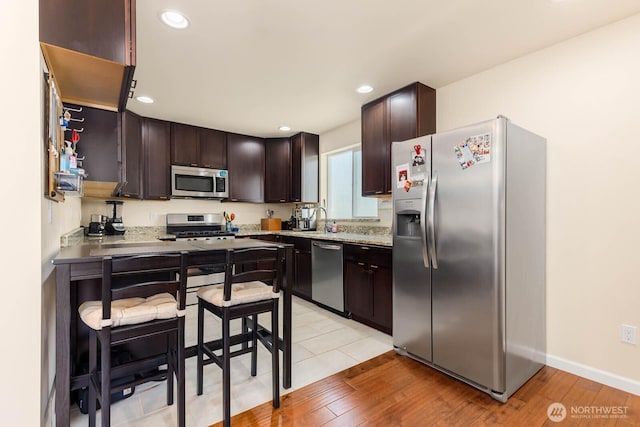 5798 Roosevelt Way NE, Seattle, WA 98105 - kitchen with appliances with stainless steel finishes, dark brown cabinets, light wood-style floors, recessed lighting, and light stone countertops