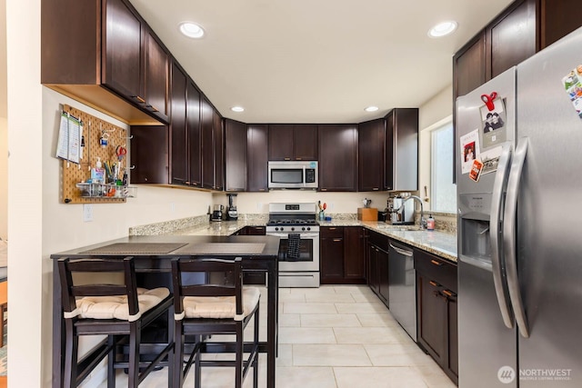 5798 Roosevelt Way NE, Seattle, WA 98105 - kitchen featuring appliances with stainless steel finishes, light stone counters, recessed lighting, dark brown cabinetry, and light tile patterned floors