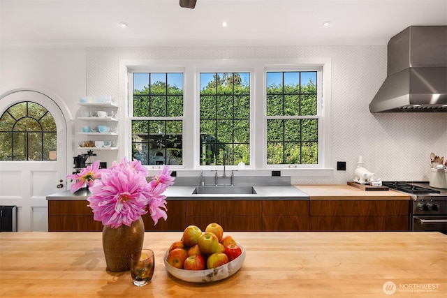 kitchen with wall chimney range hood, high end range, modern cabinets, brown cabinets, and tasteful backsplash