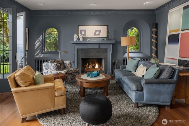 living room with wood finished floors, plenty of natural light, a tiled fireplace, and crown molding