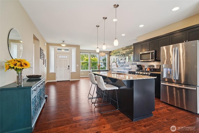 13712 Big Sky Dr E, Bonney Lake, WA 98391 - kitchen featuring stainless steel appliances, dark wood-type flooring, light stone countertops, a breakfast bar, and recessed lighting