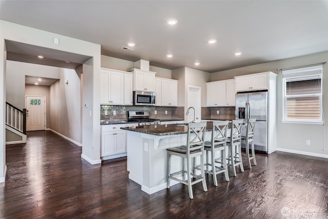 7336 Ashdown Ln SE, Olympia, WA 98513 - kitchen featuring appliances with stainless steel finishes, dark wood finished floors, an island with sink, a kitchen breakfast bar, and tasteful backsplash