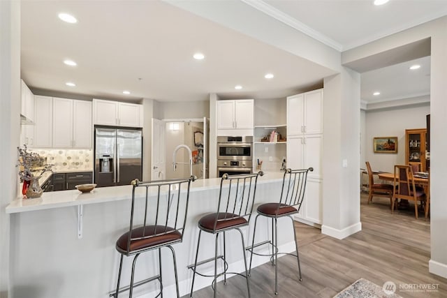 520 6th Ave Unit 2001, Kirkland, WA 98033 - kitchen featuring stainless steel appliances, crown molding, backsplash, a peninsula, and white cabinetry