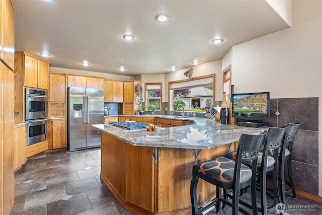 78718 Echols Rd, Hermiston, OR 97838 - kitchen with appliances with stainless steel finishes, a peninsula, light stone counters, a breakfast bar area, and backsplash