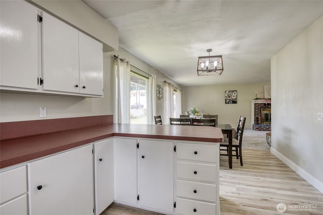 218 Holly Ln, Cosmopolis, WA 98537 - kitchen featuring a peninsula, light wood finished floors, white cabinetry, a brick fireplace, and dark countertops