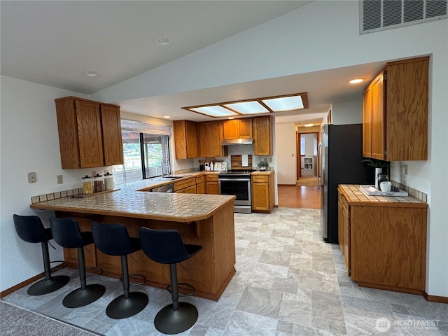 18509 22nd Ave E, Tacoma, WA 98445 - kitchen featuring stainless steel appliances, brown cabinetry, a peninsula, a breakfast bar area, and tile countertops