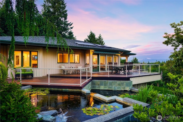 7001 Palm Ln, Anacortes, WA 98221 - back of house at dusk featuring solar panels, a wooden deck, outdoor dining area, and a pool with connected hot tub