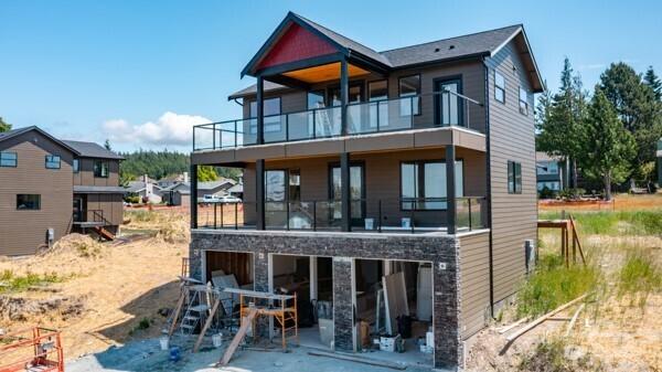 3714 W 3rd St, Anacortes, WA 98221 - back of property with a balcony, stone siding, an attached garage, and a patio
