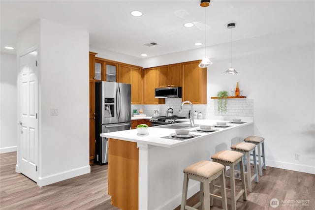 7549 SE 29th St Unit 301, Mercer Island, WA 98040 - kitchen featuring appliances with stainless steel finishes, a peninsula, brown cabinetry, a breakfast bar area, and light countertops