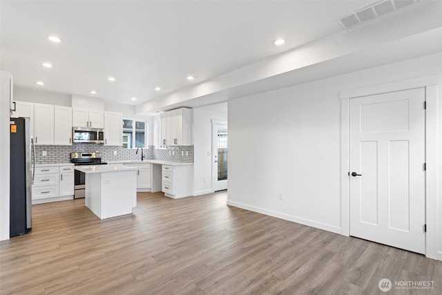 7812 S Sheridan Ave, Tacoma, WA 98408 - kitchen with stainless steel appliances, backsplash, light wood-style flooring, light countertops, and a center island