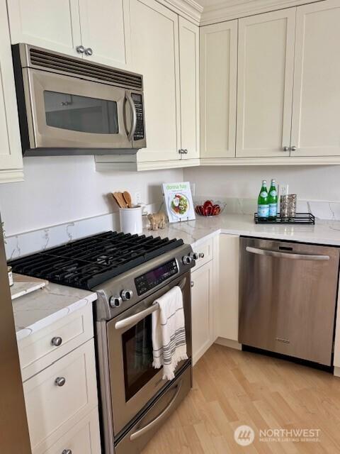 10047 Main St Unit 319, Bellevue, WA 98004 - kitchen featuring appliances with stainless steel finishes, light wood-type flooring, light stone countertops, and white cabinets