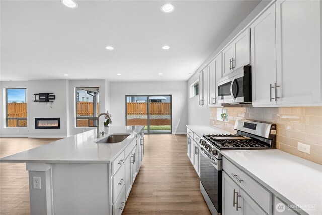 298 Hovey St, Buckley, WA 98321 - kitchen with stainless steel appliances, a glass covered fireplace, light wood-style floors, recessed lighting, and decorative backsplash