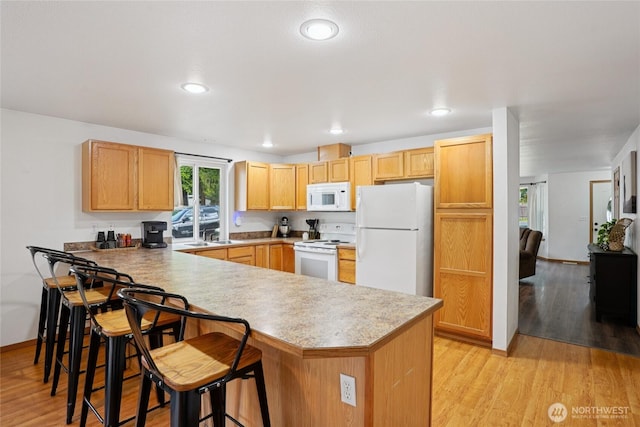 17230 Heather Ln SE, Yelm, WA 98597 - kitchen with white appliances, a peninsula, light wood-style floors, a kitchen bar, and light countertops