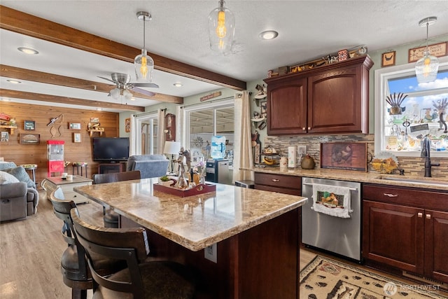 327 N Grape Dr, Moses Lake, WA 98837 - kitchen with stainless steel dishwasher, open floor plan, wood walls, light wood-style floors, and a kitchen bar