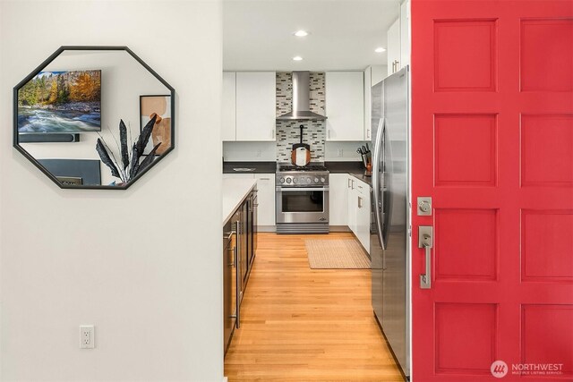 527 16th Ave W, Kirkland, WA 98033 - kitchen featuring appliances with stainless steel finishes, wall chimney exhaust hood, white cabinets, light wood-style flooring, and backsplash