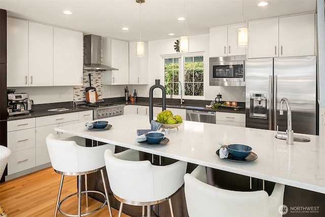 527 16th Ave W, Kirkland, WA 98033 - kitchen featuring wall chimney range hood, appliances with stainless steel finishes, a breakfast bar, decorative light fixtures, and recessed lighting