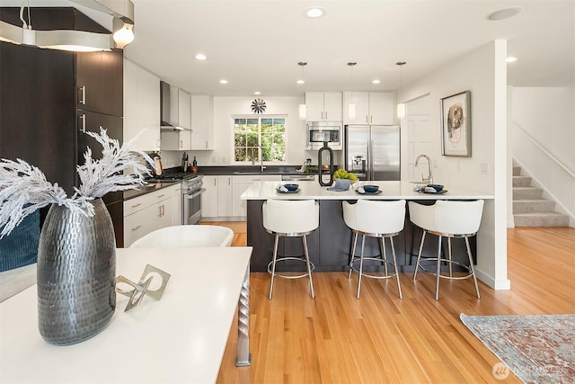 527 16th Ave W, Kirkland, WA 98033 - kitchen featuring stainless steel appliances, wall chimney exhaust hood, light wood-style flooring, a breakfast bar, and recessed lighting