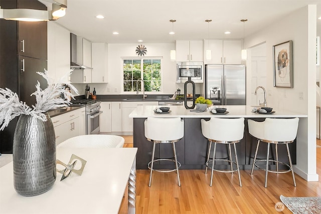 527 16th Ave W, Kirkland, WA 98033 - kitchen with stainless steel appliances, wall chimney range hood, a kitchen breakfast bar, light wood-type flooring, and recessed lighting