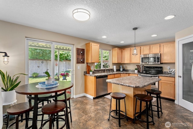 14908 NE 70th St, Vancouver, WA 98682 - kitchen featuring appliances with stainless steel finishes, light brown cabinetry, a textured ceiling, a kitchen island, and a breakfast bar