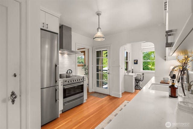 1157 N 78th St, Seattle, WA 98103 - kitchen featuring appliances with stainless steel finishes, wall chimney exhaust hood, light countertops, light wood-type flooring, and hanging light fixtures