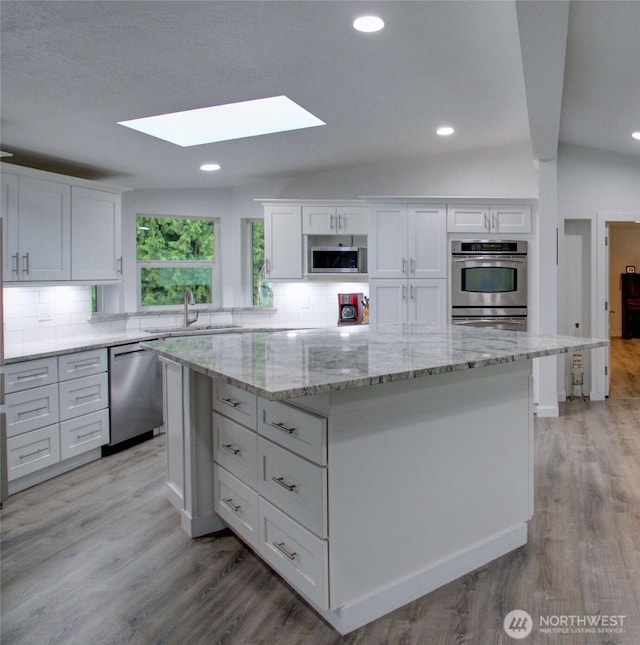 7493 State Route 9, Sedro Woolley, WA 98284 - kitchen with appliances with stainless steel finishes, a skylight, a kitchen island, white cabinetry, and decorative backsplash