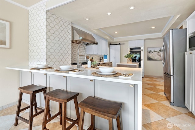 1116 N J St, Tacoma, WA 98403 - kitchen with wall chimney exhaust hood, stainless steel appliances, a peninsula, a tray ceiling, and light countertops