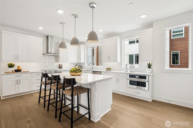 12257 137th Pl NE Unit 2901, Redmond, WA 98052 - kitchen with appliances with stainless steel finishes, wall chimney range hood, a breakfast bar, tasteful backsplash, and wood finished floors