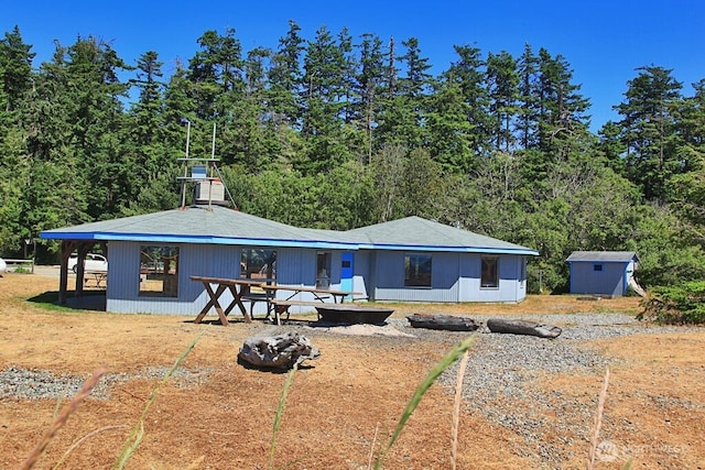 1271 Rickover Dr, Coupeville, WA 98239 - back of property featuring a fire pit, an outdoor structure, and a wooded view