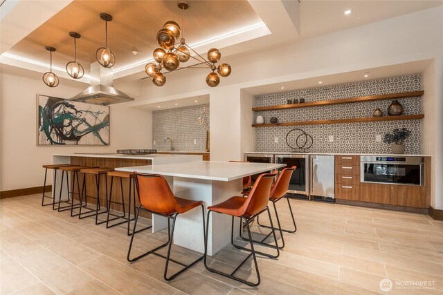 1085 103rd Ave NE Unit 217, Bellevue, WA 98004 - kitchen featuring open shelves, island range hood, a tray ceiling, stainless steel oven, and wine cooler