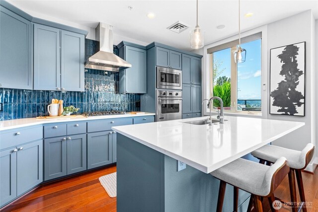 6801 Greenwood Ave N Unit 403, Seattle, WA 98103 - kitchen with wall chimney exhaust hood, appliances with stainless steel finishes, a kitchen bar, dark wood-type flooring, and decorative backsplash
